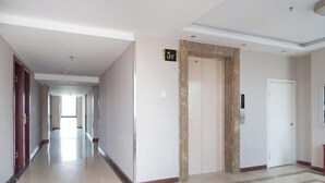 A hotel hallway with a marble floor, a door marked with a number, and a wall-mounted elevator. - Yongxiang Business Hotel (Shanghai)