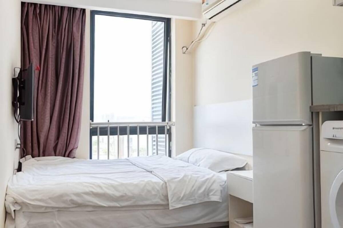 Habitació d'hotel amb llit, finestra amb cortines, nevera i rentadora.