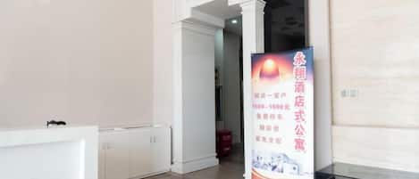 A hotel reception area with a reception desk, a vertical banner with text and a phone number, and a door leading to another room.
