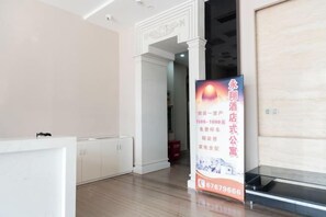 A hotel reception area with a reception desk, a vertical banner with text and a phone number, and a door leading to another room. - Yongxiang Business Hotel (Shanghai)