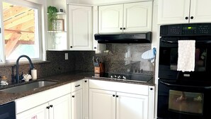 Una cocina con armarios blancos, encimera de granito, pileta de acero inoxidable, estufa negra y horno negro.