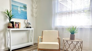 Una habitación con una consola blanca, un sillón beige, un tapete estampado y una mesita redonda con una planta.