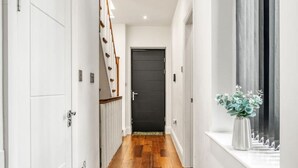 A hallway with wooden flooring, white walls, and a black door at the end. - Spacious Modern House 3BR 3BA Balcony Park View (London)