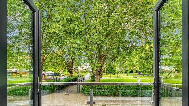 A view through a glass door of a park with trees and a pathway. - Spacious Modern House 3BR 3BA Balcony Park View (London)