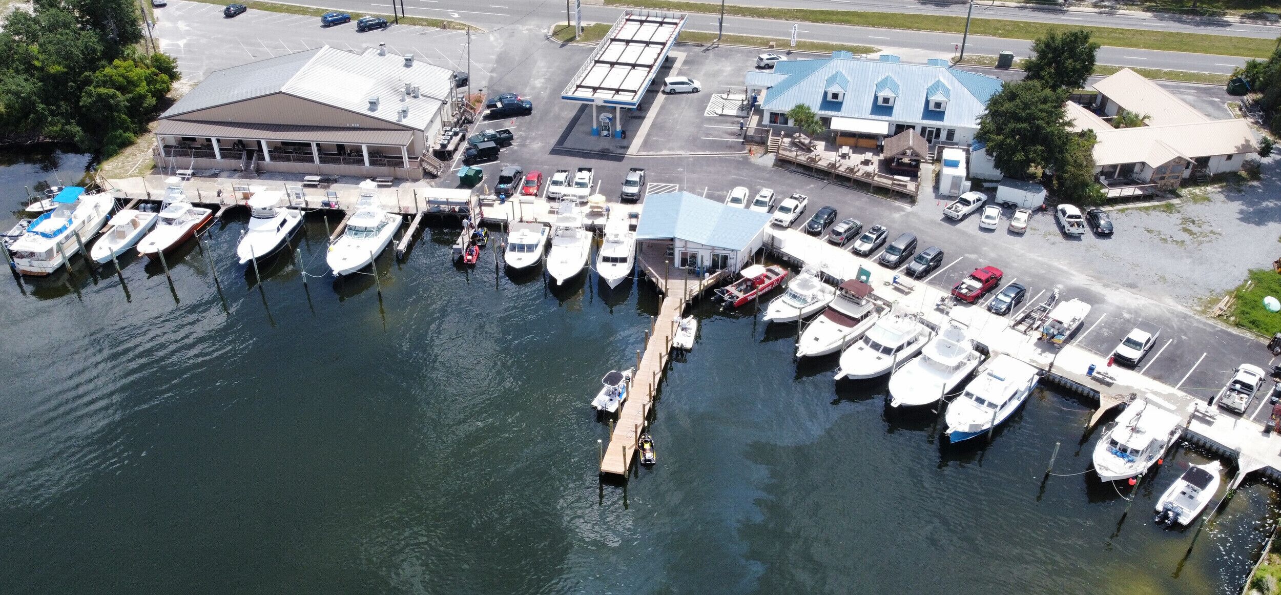An aerial view of a marina with boats docked, a fuel station, and a building with a blue roof.