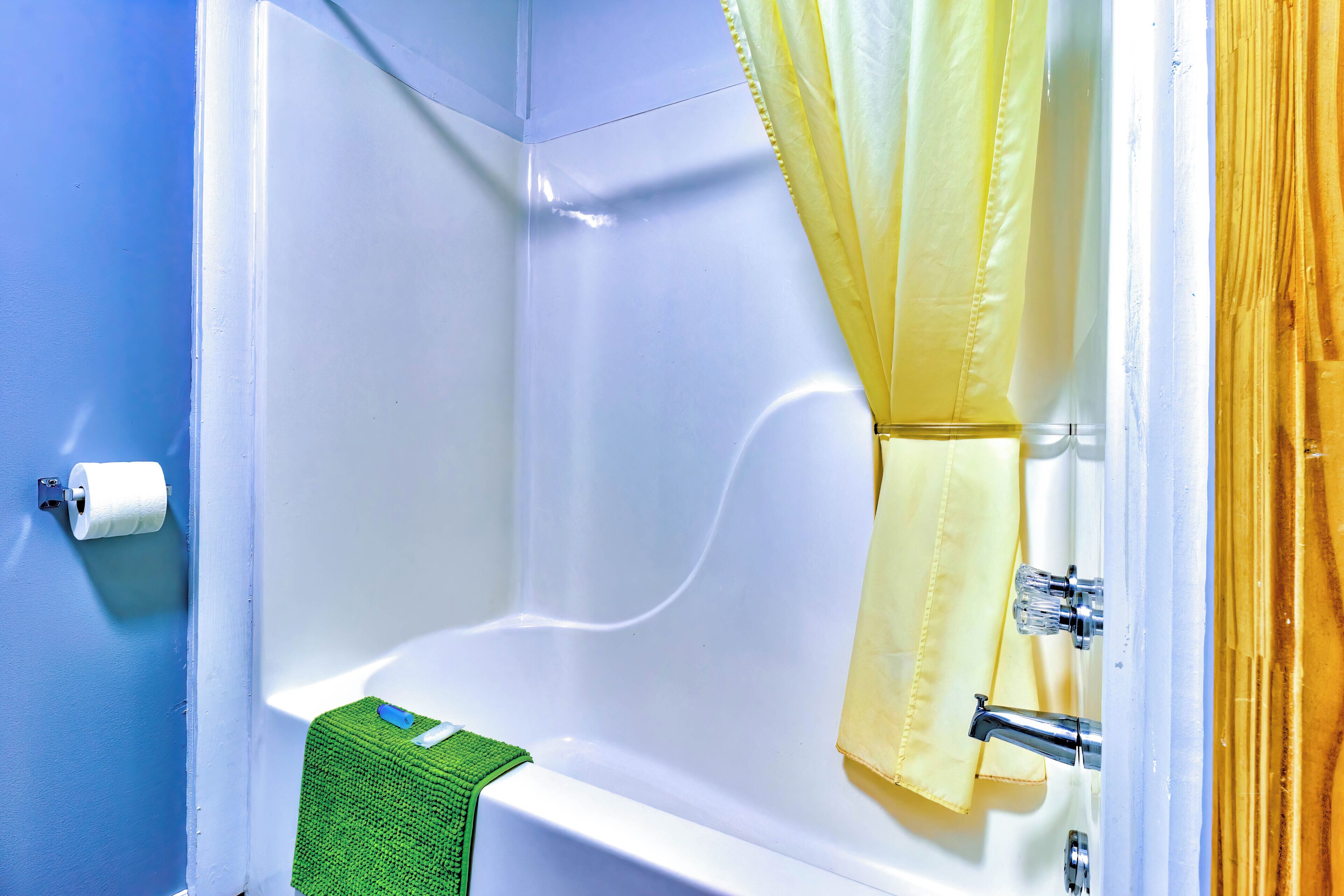 A corner bathroom with a white bathtub, a green towel, and a yellow shower curtain.