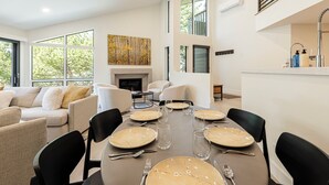 Un comedor moderno con una mesa larga dispuesta para seis personas, rodeada de sillas negras, con una chimenea y un ventanal grande al fondo.