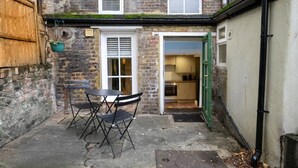 A courtyard with a table and chairs, a brick building, and a green door leading to a kitchen. - 1BR, Whitechapel, Brick Lane, Spitalfields (London)