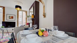 A dining area with a table set for four, a fruit bowl, and a television in the background.