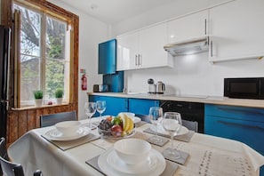 A modern kitchen with white and blue cabinets, a dining table set with plates and glasses, and a window with plants.