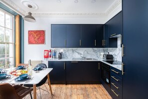A modern kitchen with dark cabinetry, a marble countertop, and a dining area with a table set for two.