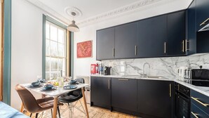 A modern kitchen with dark cabinets, a marble countertop, and a dining area with a table set for four. - Stunning luxury flat in Prime Central London (London)