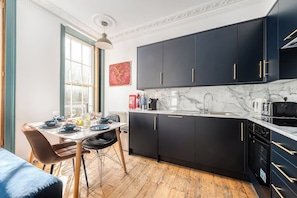 A modern kitchen with dark cabinets, a marble countertop, and a dining area with a table set for four.