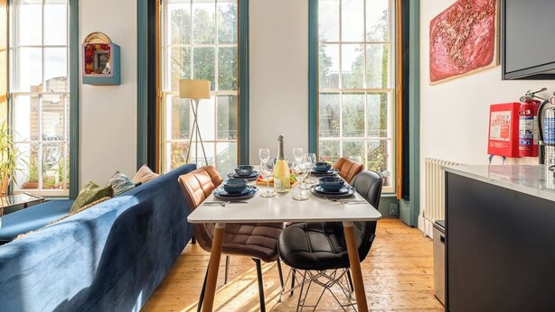 A dining area with a table set for four, a sofa, and a fire extinguisher on the wall. - Stunning luxury flat in Prime Central London (London)