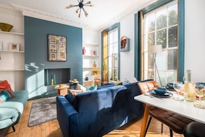 A modern living room with a blue sofa, a dining table, and a fireplace.