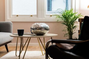 Een kamer met een ronde tafel, een stoel, een kamerplant en een raam met jaloezieën.