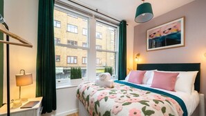A bedroom with a bed, a bedside table, a lamp, a window with curtains, and a painting on the wall.