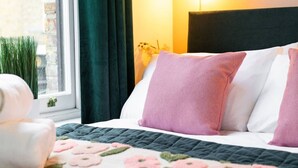 Una cama con colcha, almohadas, una mesita de noche, una lámpara y una ventana con cortinas.