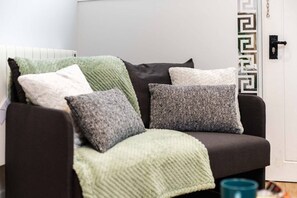 A dark-colored sofa with a green knitted throw blanket and several pillows in various shades and textures.