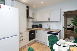 A compact kitchen with white cabinets, a microwave, a dishwasher, and a dining area with a table set for two. - Stylish Finsbury Park Flat | Lounge | Fast WiFi (London)