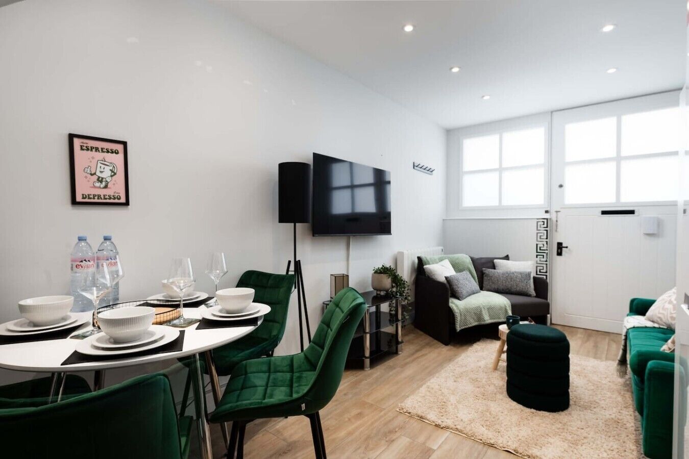 A modern living room with a dining area, green chairs, a flat-screen TV, and a large window.