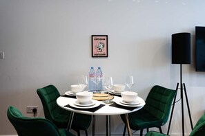 A dining area with a round table, green chairs, white plates, glasses, and water bottles. - Stylish Finsbury Park Flat | Lounge | Fast WiFi (London)