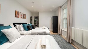 A modern bedroom with two beds, a radiator, and a window with curtains. - Stylish Finsbury Park Flat | Lounge | Fast WiFi (London)