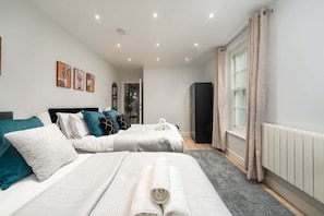 A modern bedroom with two beds, a radiator, and a window with curtains. - Stylish Finsbury Park Flat | Lounge | Fast WiFi (London)