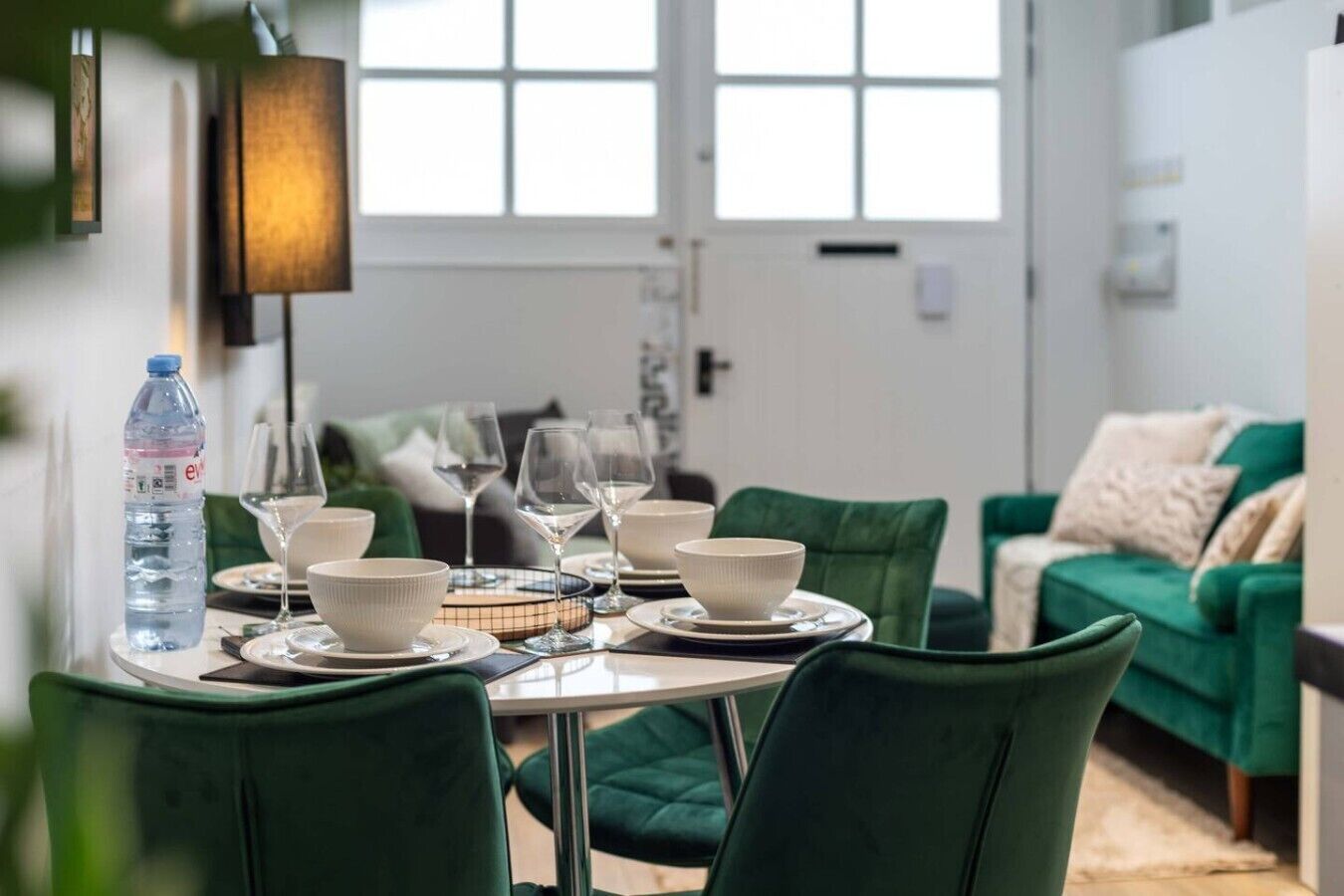 A dining area with a table set for four, green upholstered chairs, and a water bottle on the table.