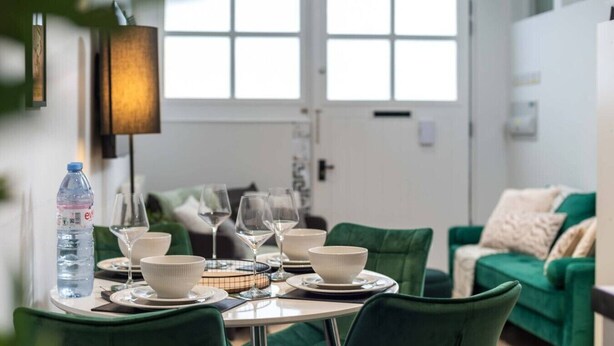 A dining area with a table set for four, green upholstered chairs, and a water bottle on the table. - Stylish Finsbury Park Flat | Lounge | Fast WiFi (London)