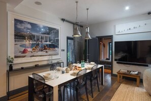 A dining area with a large table, chairs, a TV, and a painting of a pool scene.
