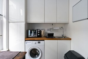 A compact kitchen with a washing machine, a coffee maker, and a microwave on the countertop.