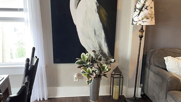 A living room with a large painting of a bird, a potted plant, a floor lamp, and a sofa. - 3-bedroom duplex yellow house downtown  Des Moines with AC, WiFi (des moines)