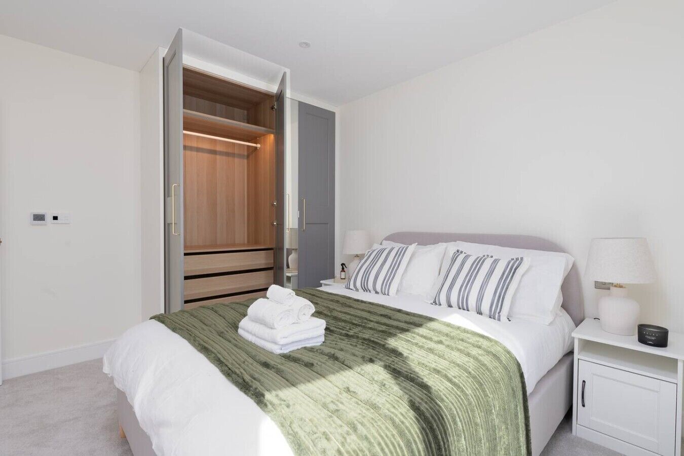 Une chambre à coucher avec un lit, une table de chevet, une lampe, une armoire et un miroir.