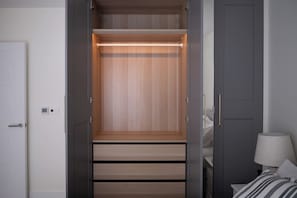 Ein begehbarer Kleiderschrank mit Schiebetüren, eine Lampe und ein Bett mit gestreifter Bettdecke.