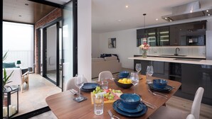 A modern dining area with a wooden table set for four, a kitchen with stainless steel appliances, and a sliding glass door leading to a balcony. - Fast Wifi, Winter Balcony, Chef`s Kitchen, Fulham (London)