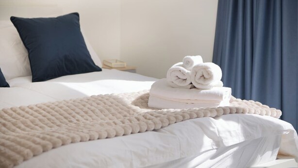 Un letto rifatto con lenzuola bianche, un cuscino blu scuro e una coperta beige.