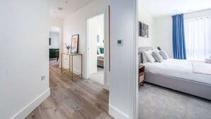 Una habitación de hotel moderna con una cama grande, una mesita de noche y vistas al pasillo.