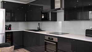 Une cuisine moderne avec des meubles de couleur sombre, une hotte de cuisine en acier inoxydable, un lave-vaisselle encastré et un plan de travail blanc.