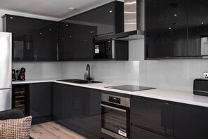 Cocina moderna con armarios oscuros, campana extractora de acero inoxidable, lavavajillas integrado y encimera blanca.