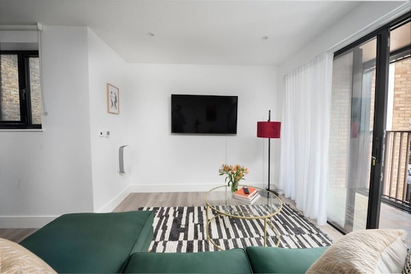 A modern living room with a sofa, a flat-screen TV, a red floor lamp, and a patterned rug.