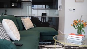 A modern living room with a green sofa, a glass coffee table, and a small bookshelf.