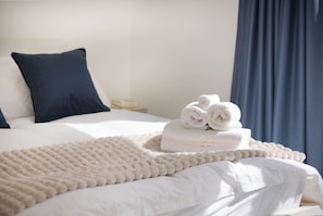 A neatly made bed with white linens, a dark blue pillow, and a beige throw blanket.
