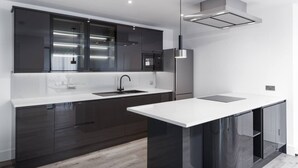 A modern kitchen with dark cabinetry, a white countertop, a stainless steel refrigerator, and a pendant light.