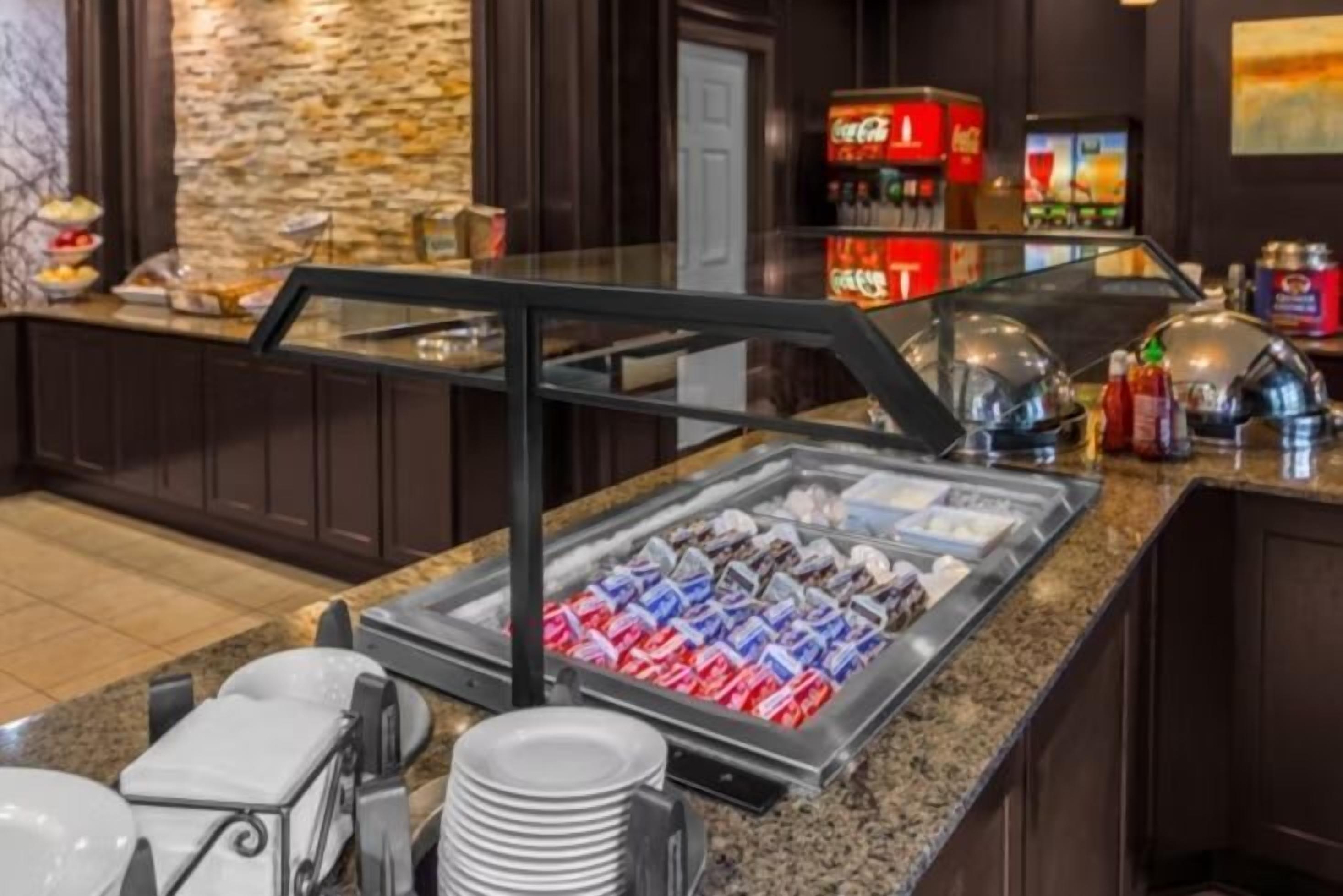 Un espace buffet doté d’une vitrine réfrigérée où sont présentés divers aliments, d’un coin café et d’un comptoir avec un distributeur de boissons.