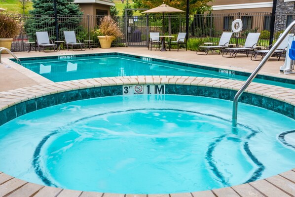 Una piscina rectangular con borde de azulejos, rodeada de sillas de descanso y una valla.