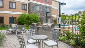 Eine Terrassenanlage im Freien mit Grill, Sitzgelegenheiten und Blick auf ein Schwimmbad.
