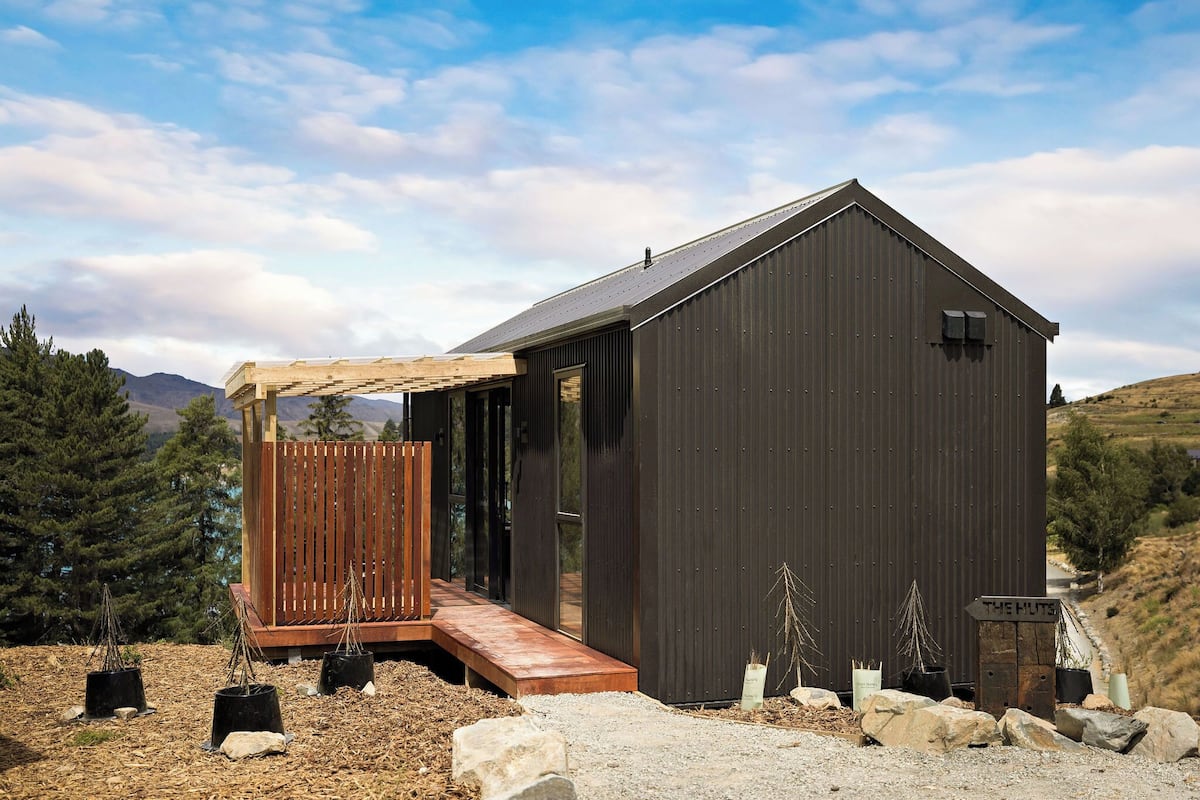 En moderne bygning med en træterrasse og et skilt, der viser "THE HUTS".