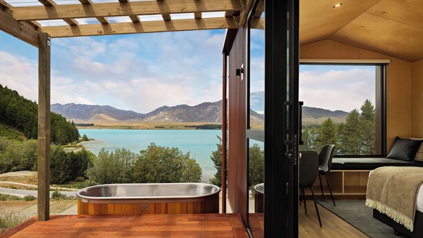 Une chambre avec une grande fenêtre, un plafond en bois et une vue sur un lac et des montagnes.