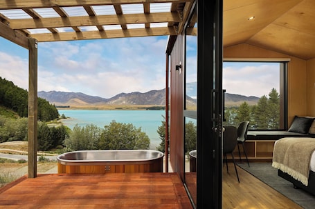 A bedroom with a large window, a wooden ceiling, and a view of a lake and mountains.